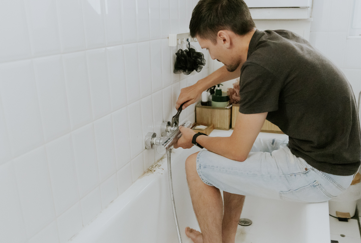 Man repairing bathtub faucet for walk in shower vs bathtub comparison
