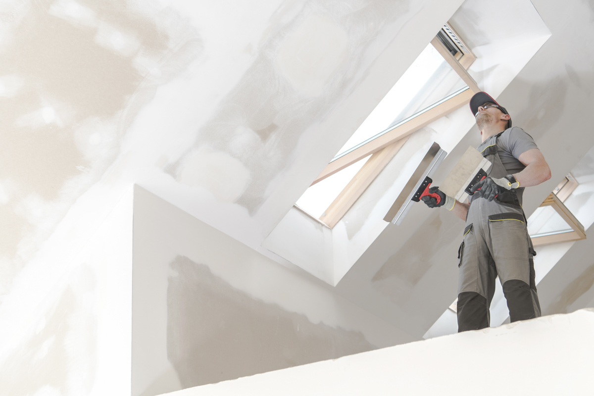 Contractor finishing drywall around impact windows installation
