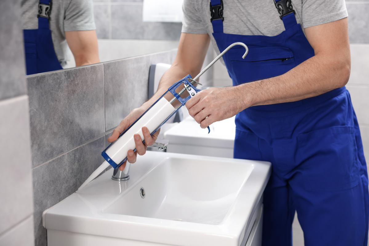 Contractor sealing bathroom tile flooring near vanity sink