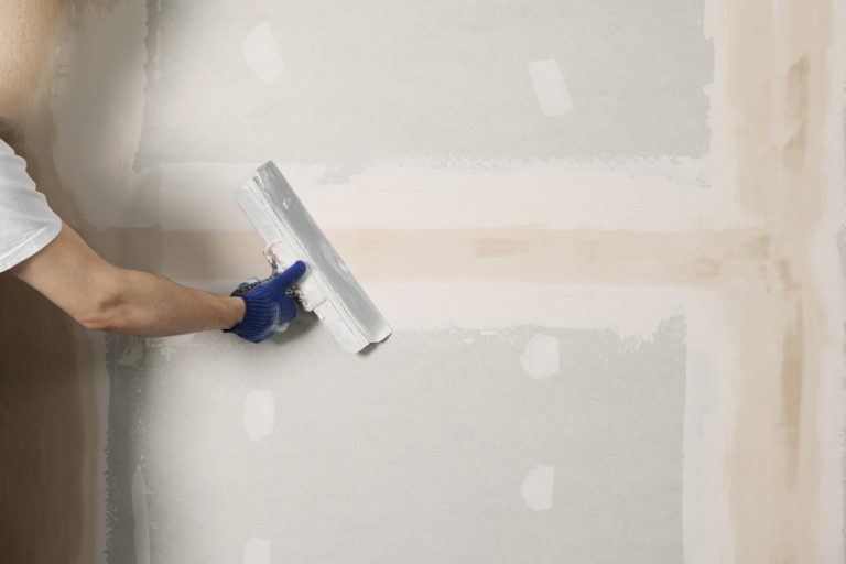 Contractor smoothing drywall anchor hole repair with putty knife