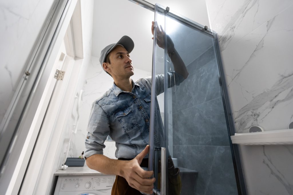 Contractor installing glass shower door in marble bathroom renovation