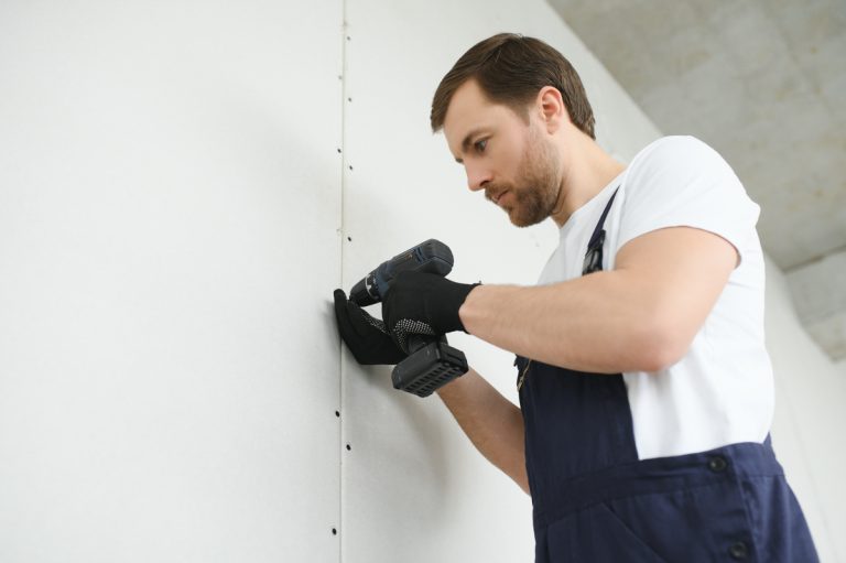 Contractor installing drywall panel, affecting drywall repair cost