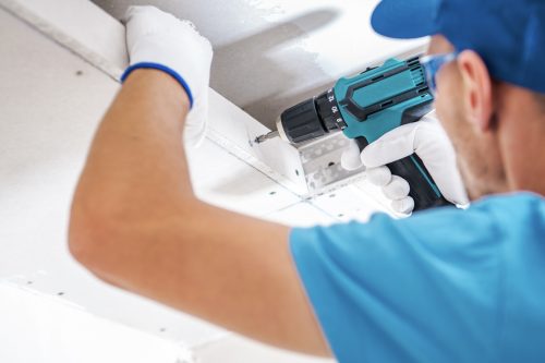 Contractor performing water damage ceiling repair with drill
