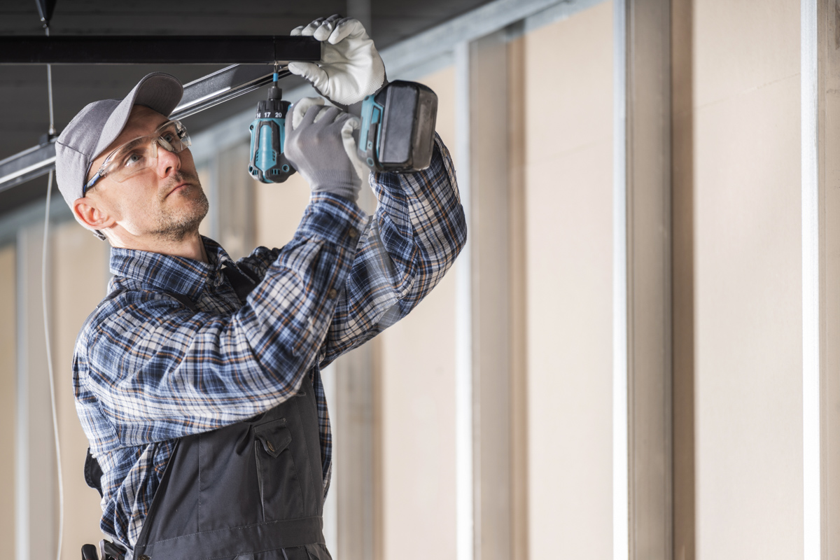 Contractor repairing ceiling water damage with a power drill