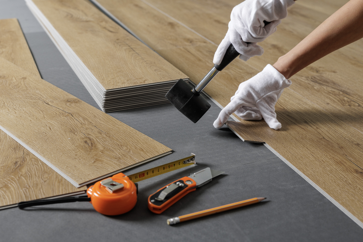 Installer fitting wood-look luxury vinyl plank flooring with mallet