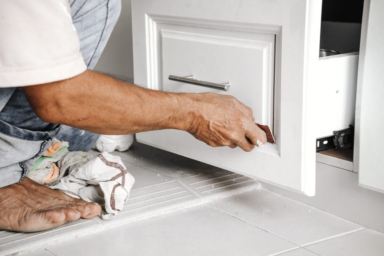 Contractor sanding a white kitchen cabinet door during installation