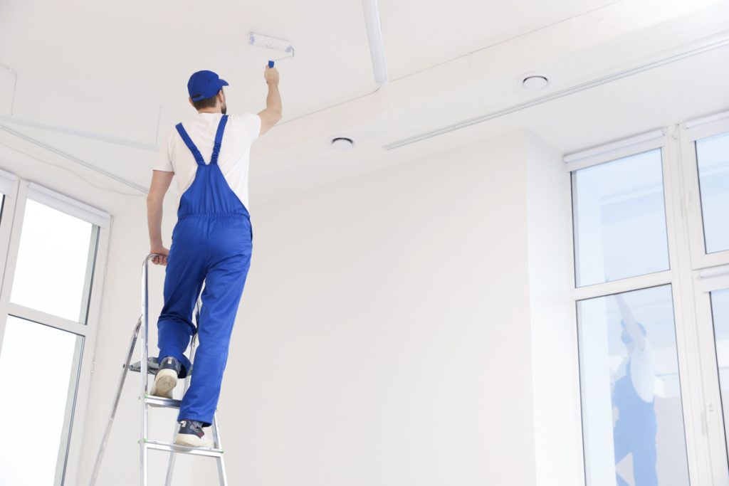 Contractor painting ceiling in bright room with vinyl plank flooring